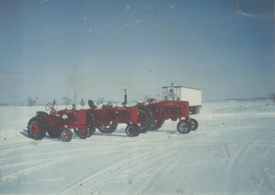 Three red tractors outside of shed during winter